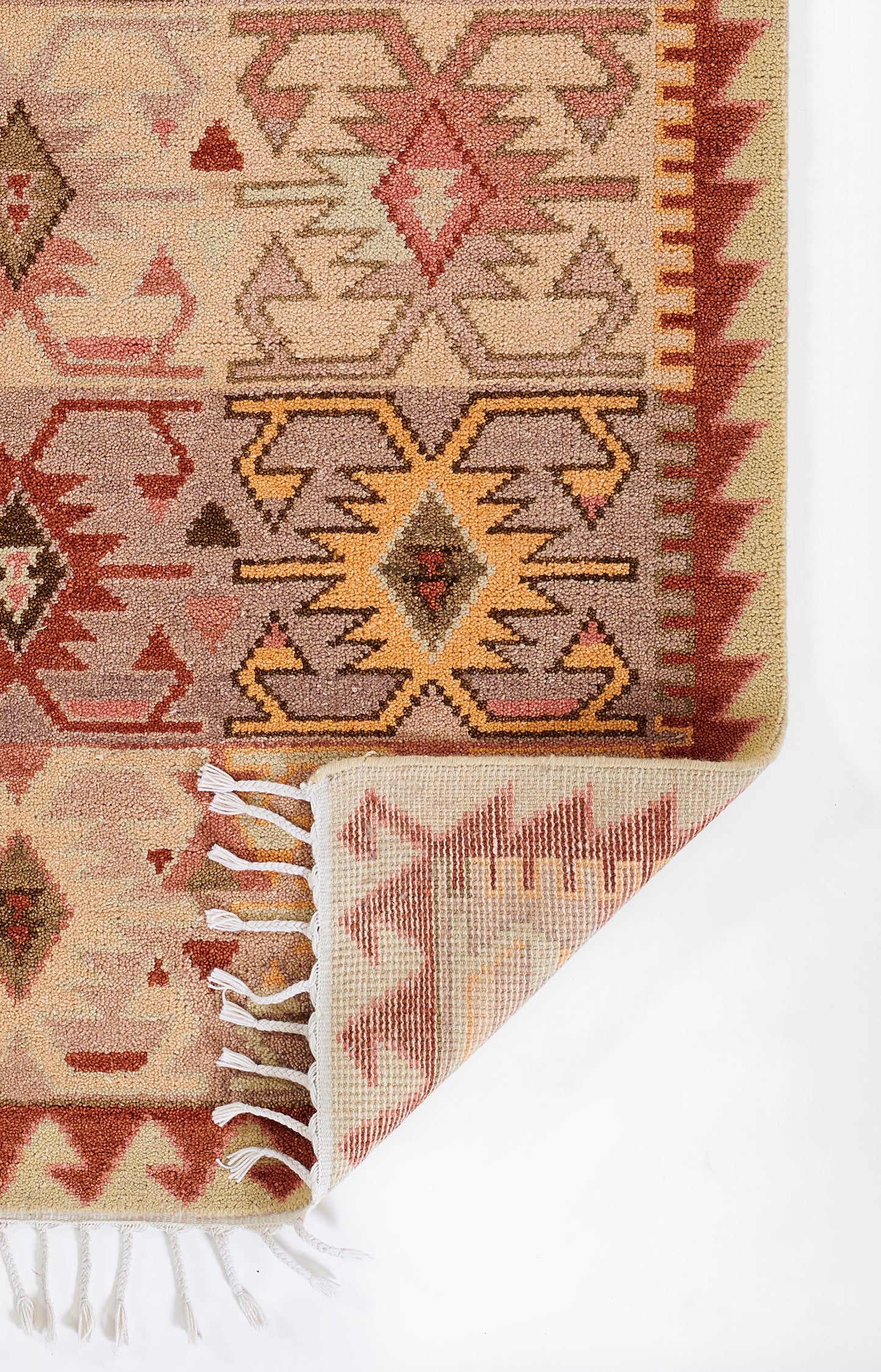 Geometric kilim-style rug in warm beige with rust, pink and orange tribal motifs; woven wool, fringed edges, rolled corner.
