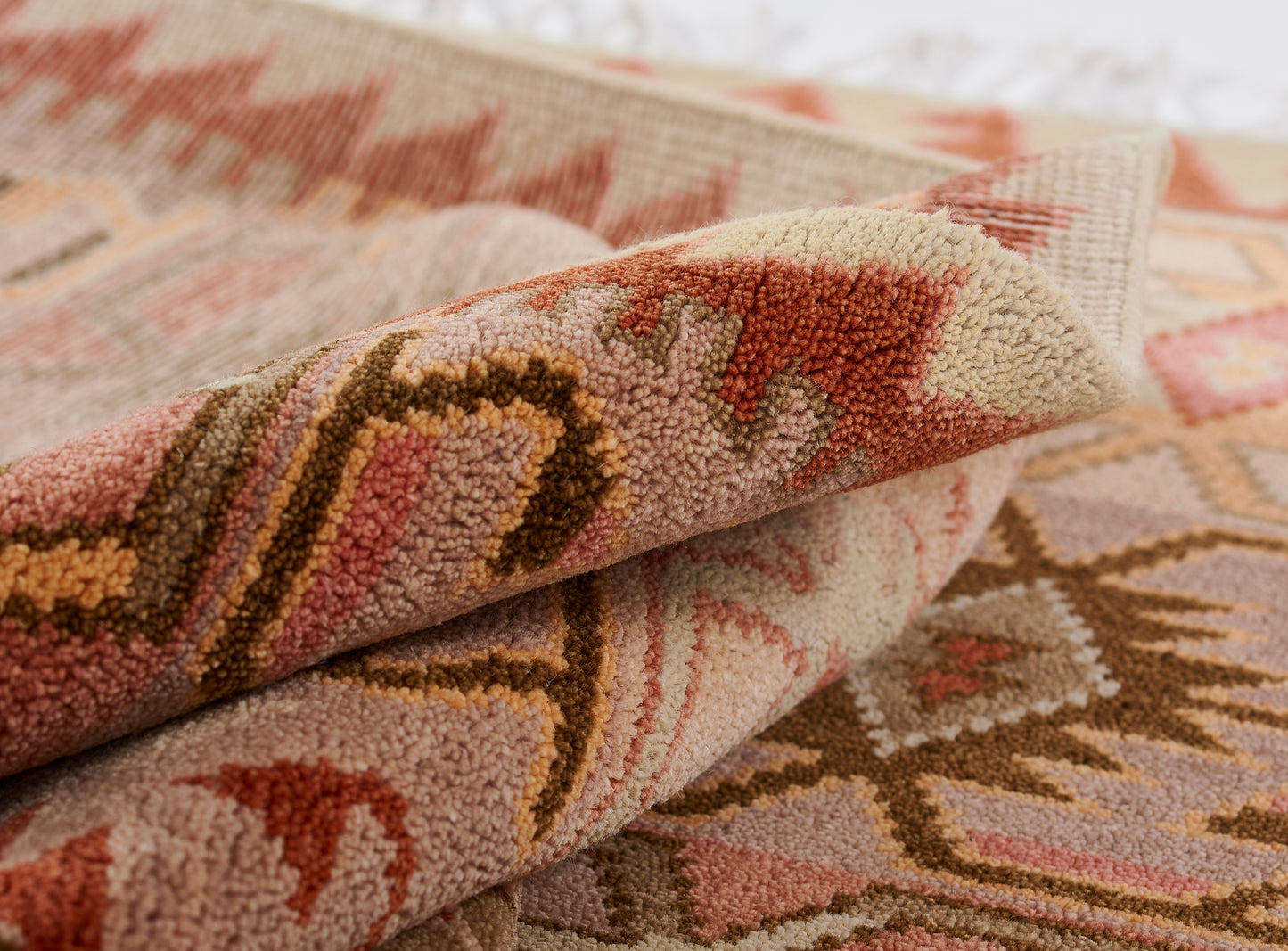 Nomad rug: close-up of folded tribal kilim with pink, peach, beige and brown geometric patterns and plush pile.