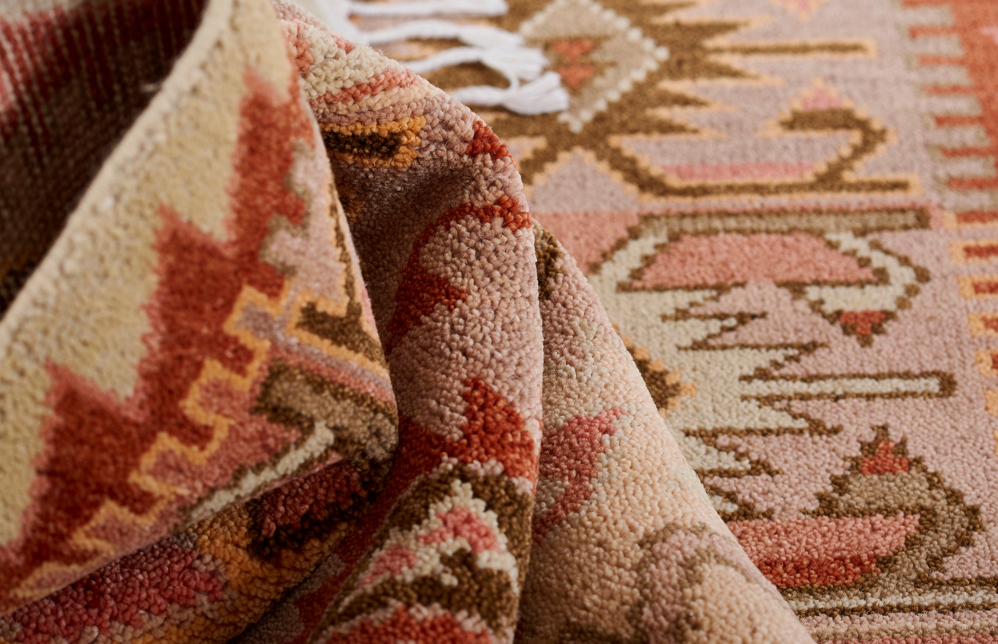 Soft pink and cream geometric rug with tan, rust and peach accents; woven pile, fringe along edge.