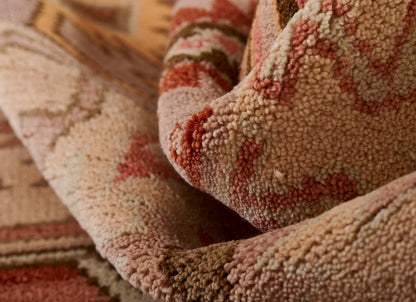 Close-up of a plush Nomad-style rug with a thick pile in warm beige, pink, red and rust tones.