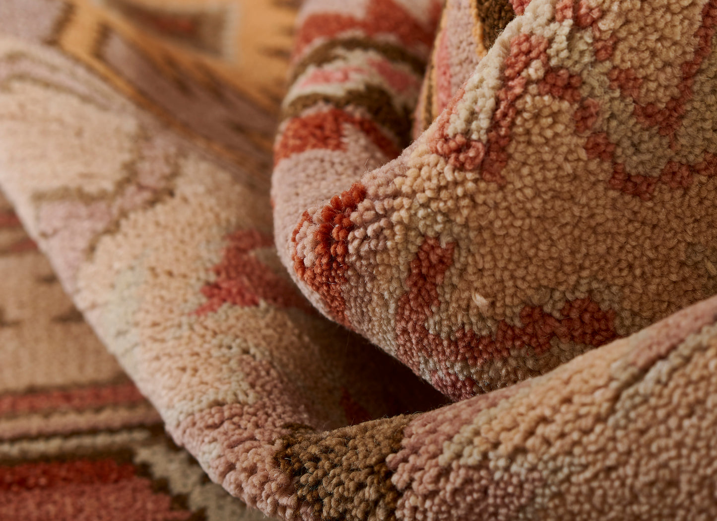 Close-up of a plush tufted rug in earthy tones - blush pink, rust, beige and cream with a floral pattern.
