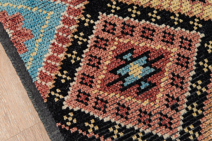 Close-up of a nomad-style geometric rug with red, black, blue & cream tones on a wooden floor.