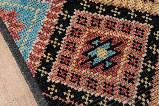 Close-up of a nomad-style geometric rug with red, black, blue & cream tones on a wooden floor.