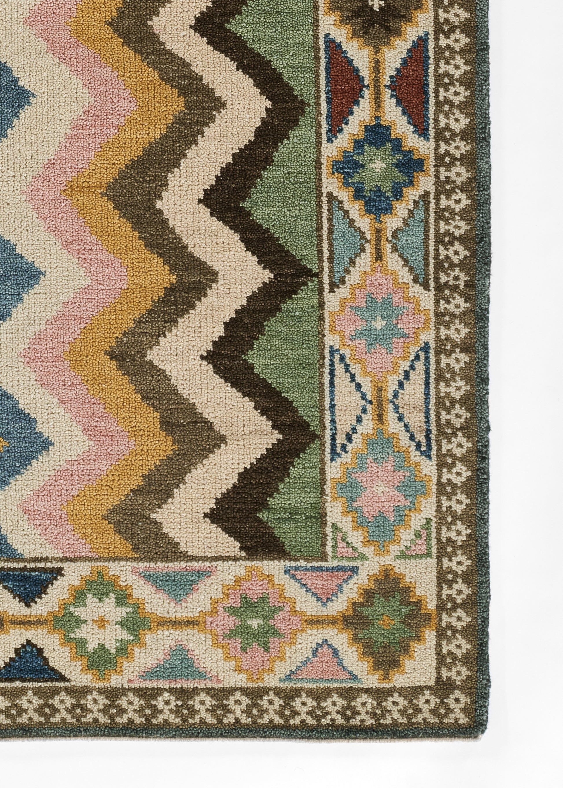 Nomad-style wool area rug with bold chevron zigzags in green, cream, brown, pink and blue; ornate bordered motif.