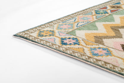 Corner view of a vibrant geometric nomad rug with pastel diamonds, greens, pinks, blues, yellow, beige border and pink fringe.