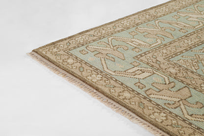 Rectangular rug with pale teal field, tan borders and geometric motifs; cream fringe along the edge.