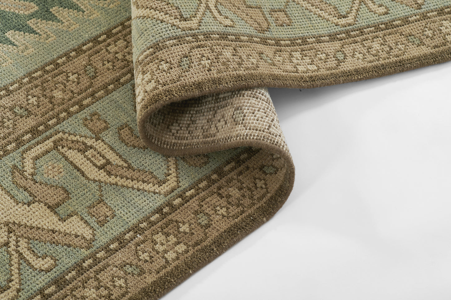 Teal & beige oriental rug with brown border, rolled at edge, dense knotted pile & classic geometric pattern.