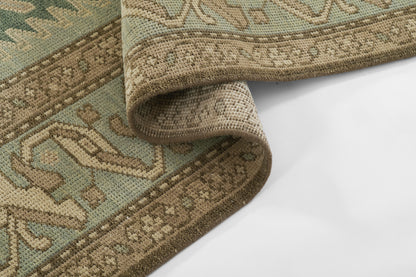 Teal and beige oriental-style woven rug with decorative border, rolled corner showing underside.