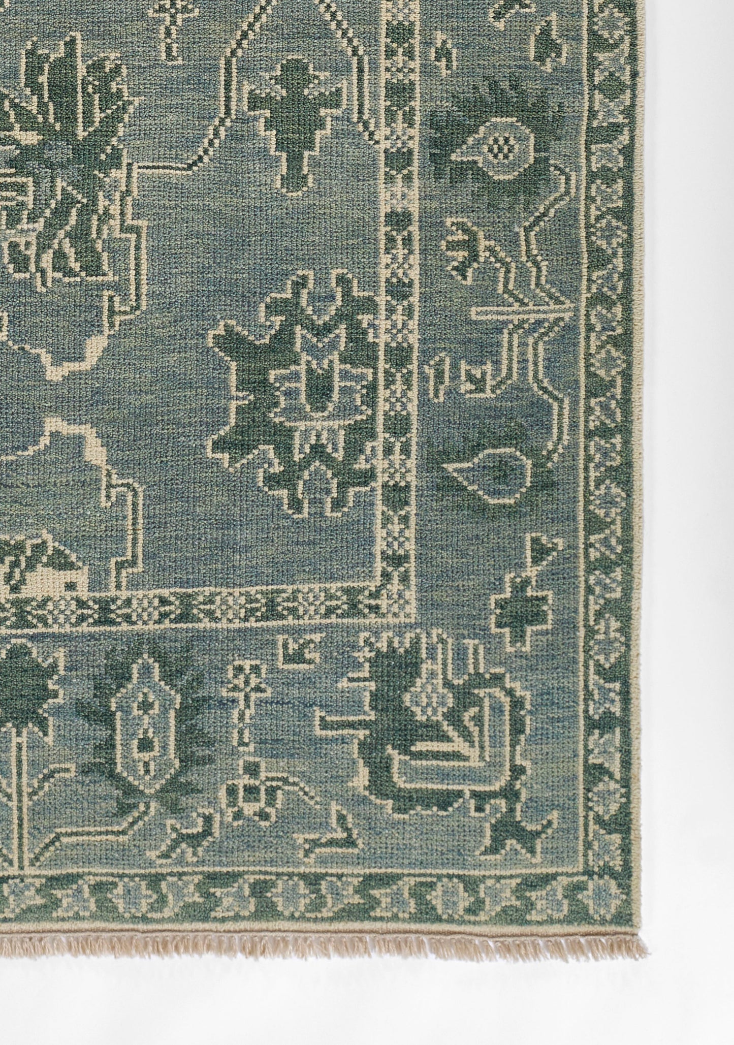 Blue-green oriental rug with cream geometric floral motifs and a fringed border.
