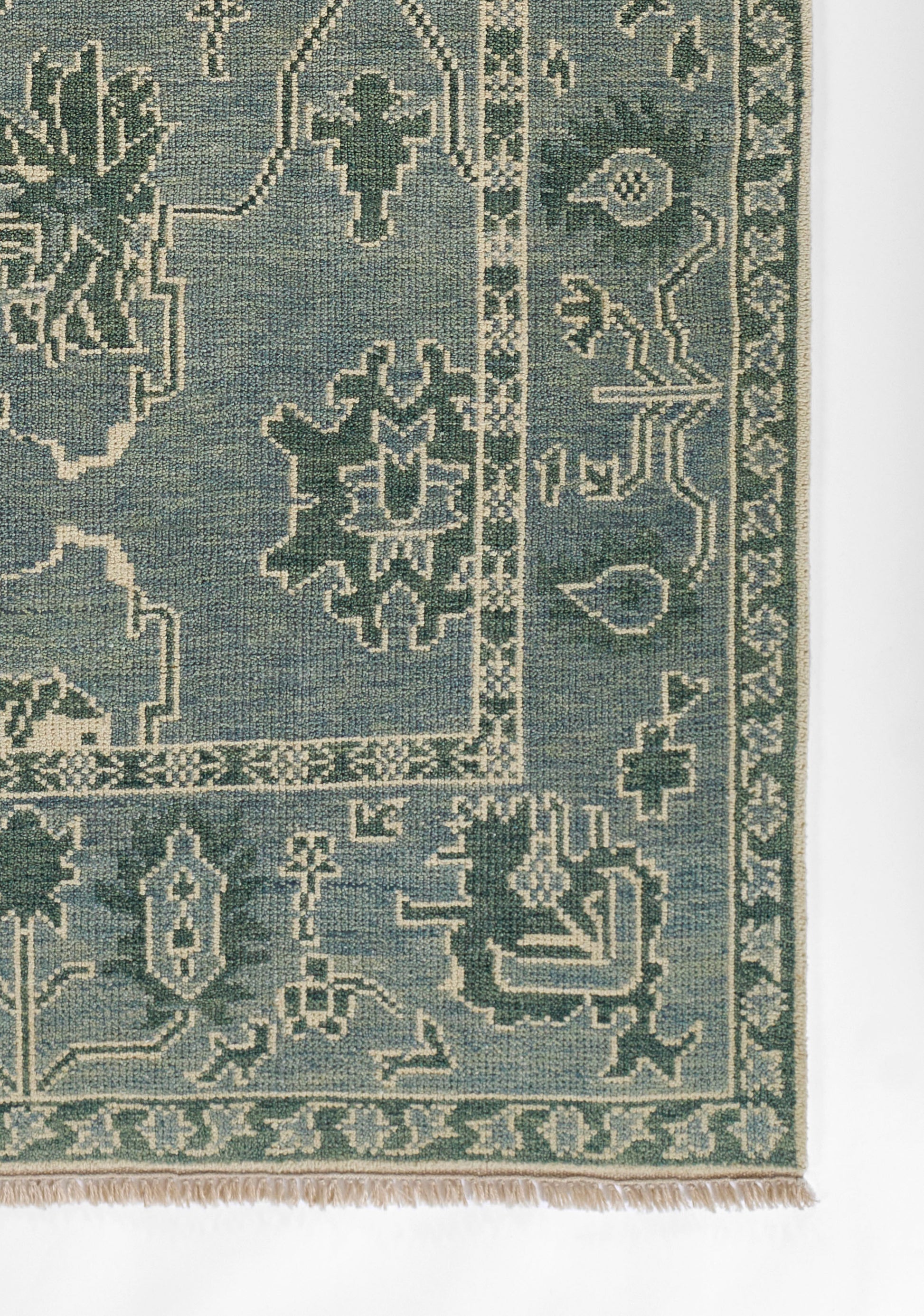 Blue-green oriental rug with cream geometric floral motifs and a fringed border.