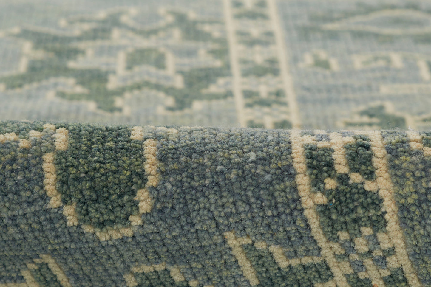Close-up of a blue-green rug with beige geometric motifs and a soft plush pile.
