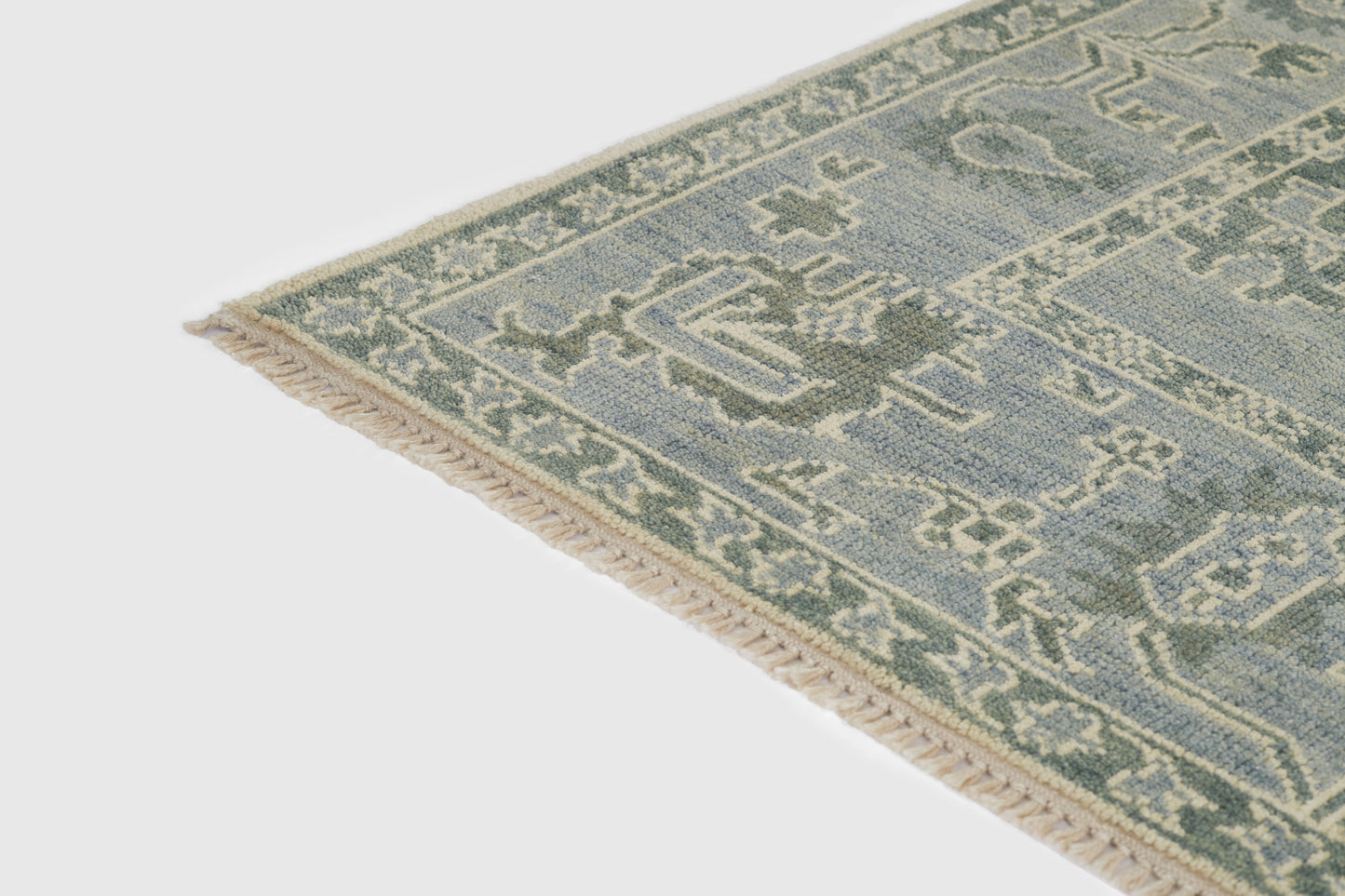 Blue and sage-green oriental rug corner with cream fringe and geometric border.