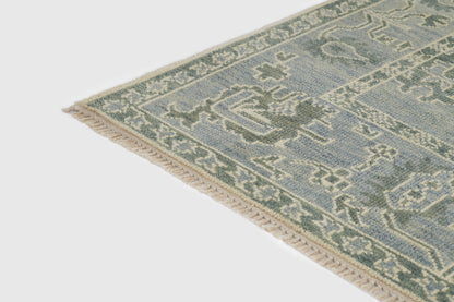 Blue and sage-green oriental rug corner with cream fringe and geometric border.