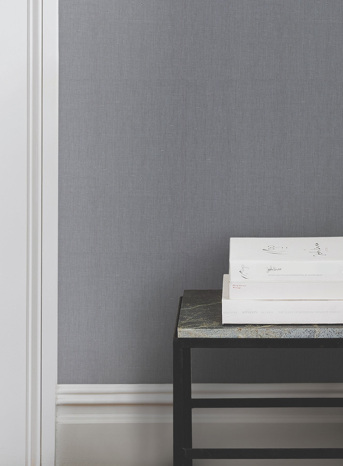 Blue crosshatch wallcovering on wall, white baseboard, black metal side table with stone top, stacked white books.