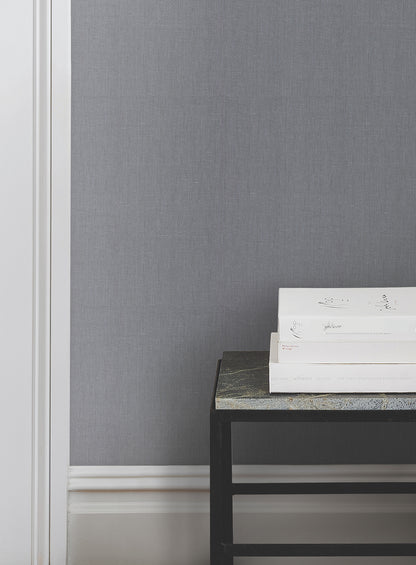 Blue crosshatch wallcovering on wall, white baseboard, black metal side table with stone top, stacked white books.