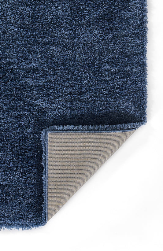Navy blue shag rug with thick fluffy pile; folded corner reveals beige woven backing.