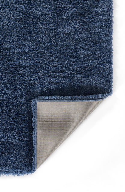 Navy blue shag rug with plush pile; corner folded to show beige fabric backing and blue fringe edge.