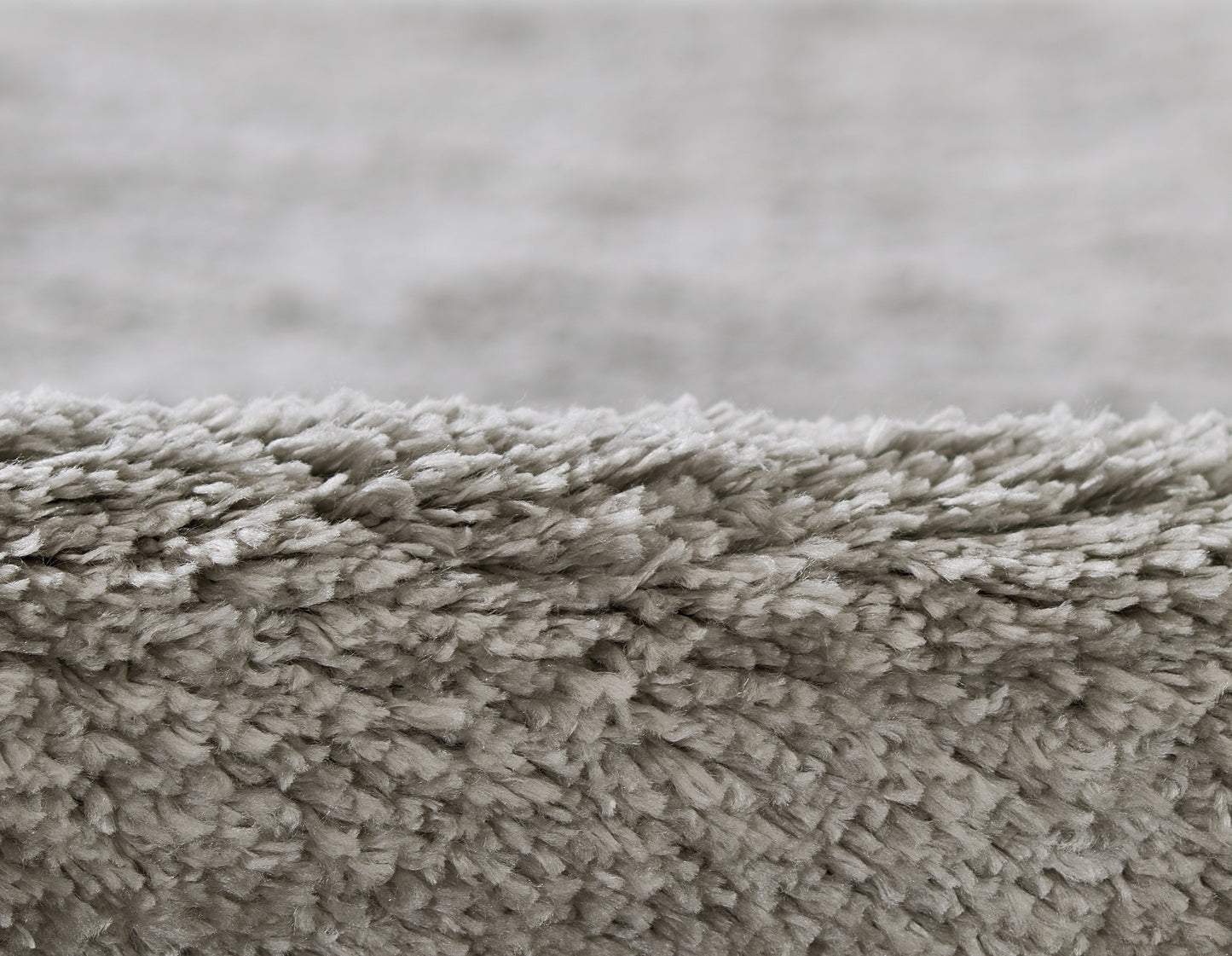Close-up of a light gray shag rug edge with dense, plush pile and soft texture.