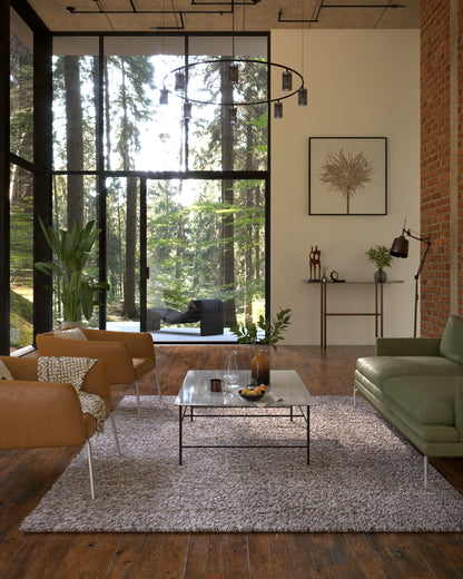 Sunlit modern living room with floor-to-ceiling glass, tan leather chairs, green sofa, gray shag rug, glass coffee table.