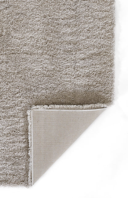 Taupe shag rug with plush pile; folded corner reveals beige backing with grid weave and fringe.