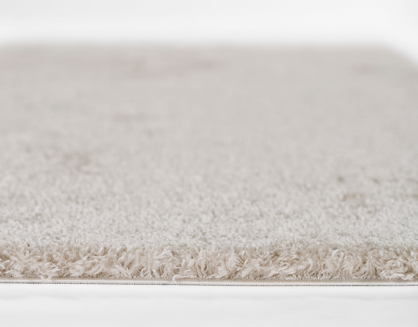 Beige plush shag rug with ultra-soft pile and fringe-edge, neutral tones for living room or bedroom decor.