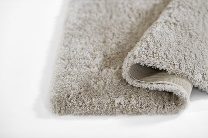 Beige shag rug with plush pile, thick rectangular area rug, rolled edge reveals non-slip backing; cozy floor mat.