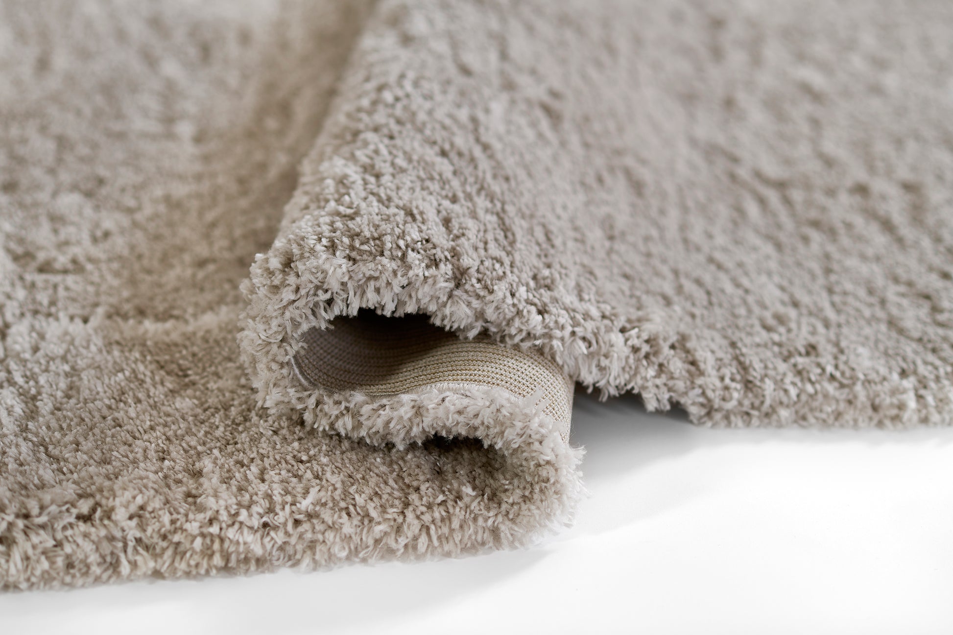 Beige shag rug with plush long pile; rolled edge reveals woven underside.