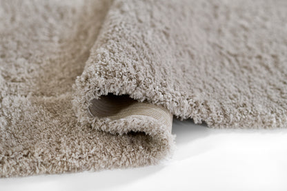 Beige shag rug with plush long pile; rolled edge reveals woven underside.