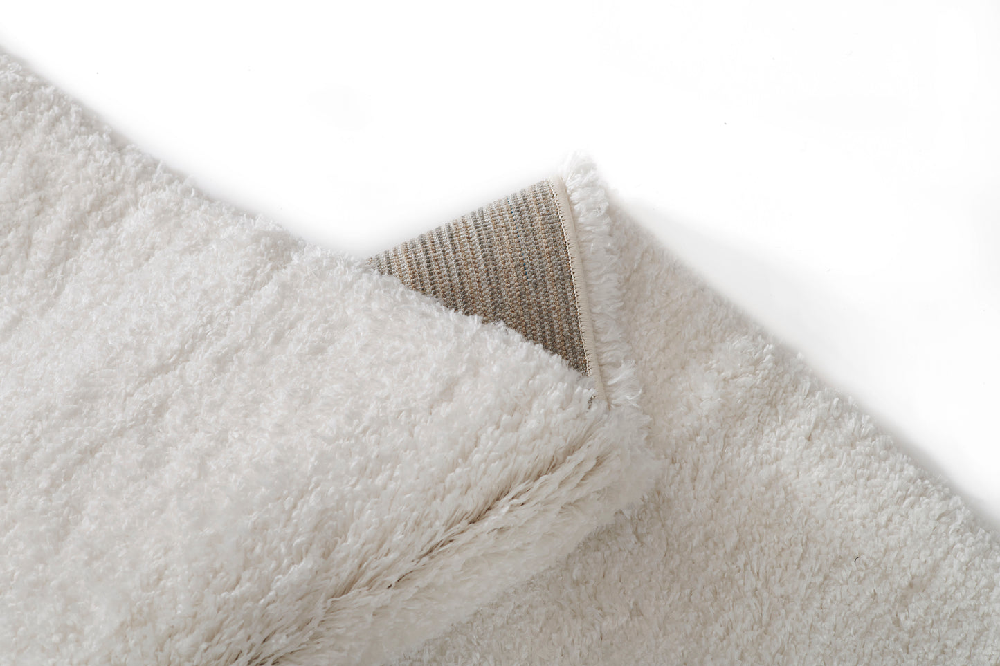 White fluffy shag rug with ultra-soft pile, beige woven underside peeking from corner.