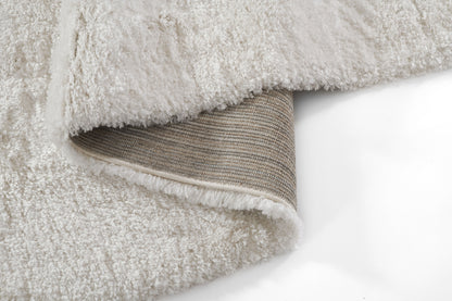Cream shag rug with plush pile; folded edge reveals beige striped woven backing and white binding.