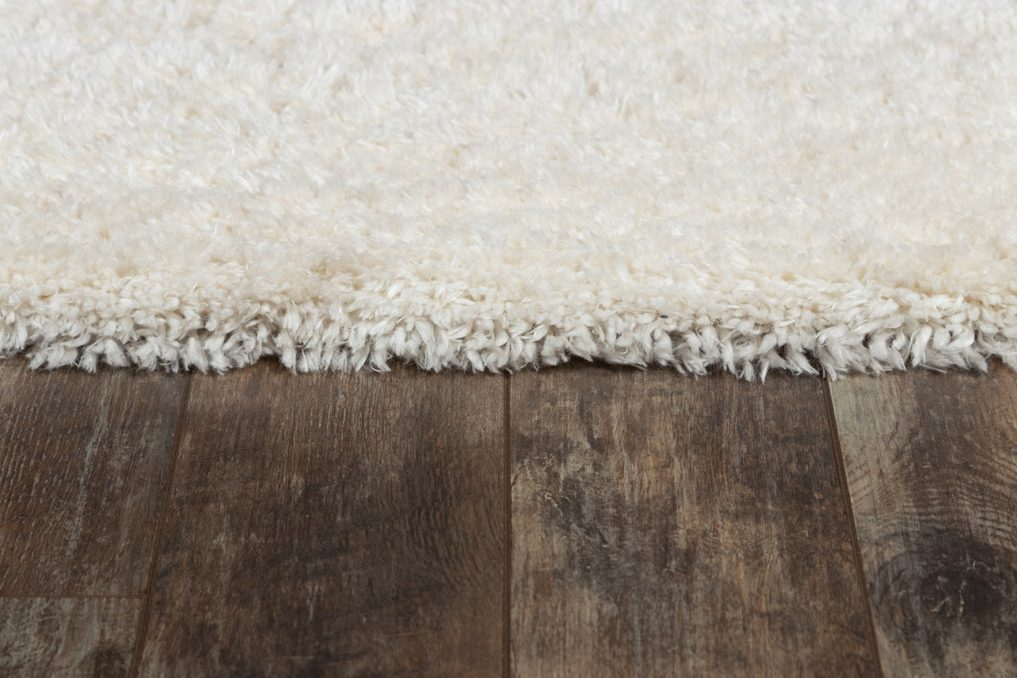 Cream white shag rug edge with fluffy pile and fringe on dark wooden floor.