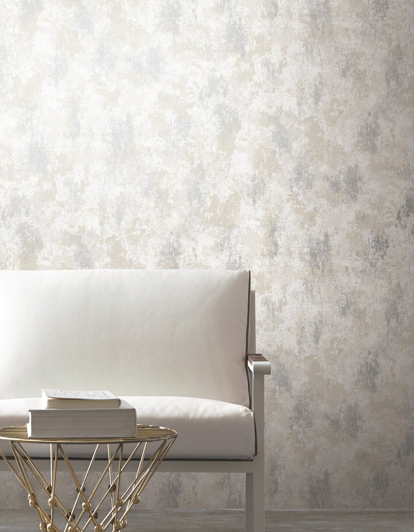 White modern lounge chair with metal arms beside a gold geometric wire-frame side table and stacked books.