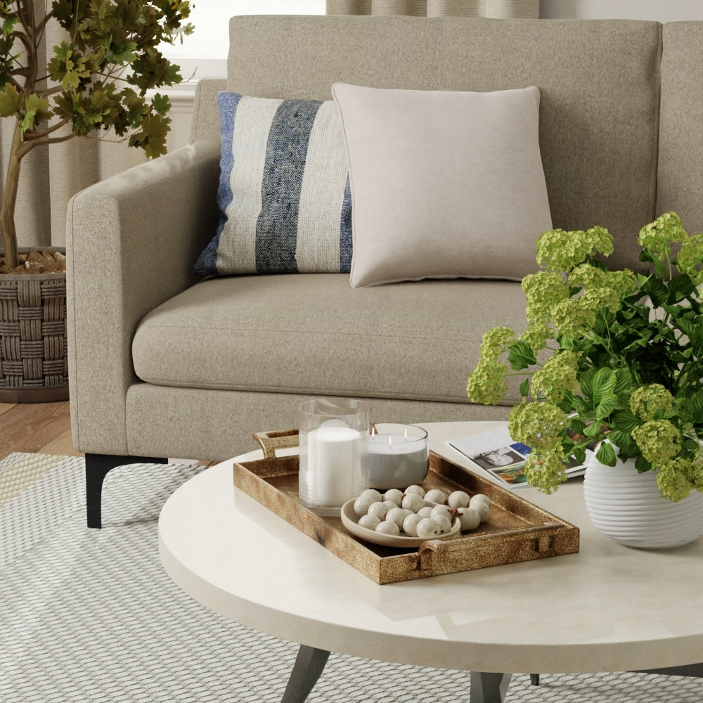 Beige fossil solid fabric upholstery on a sofa with striped and solid cushions, and a round marble coffee table with a wooden tray of candles and stones.