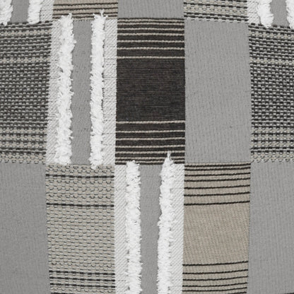 Outdoor pillow with patchwork grey, black, and beige woven fabric featuring striped and textured blocks in a quilt-like pattern.