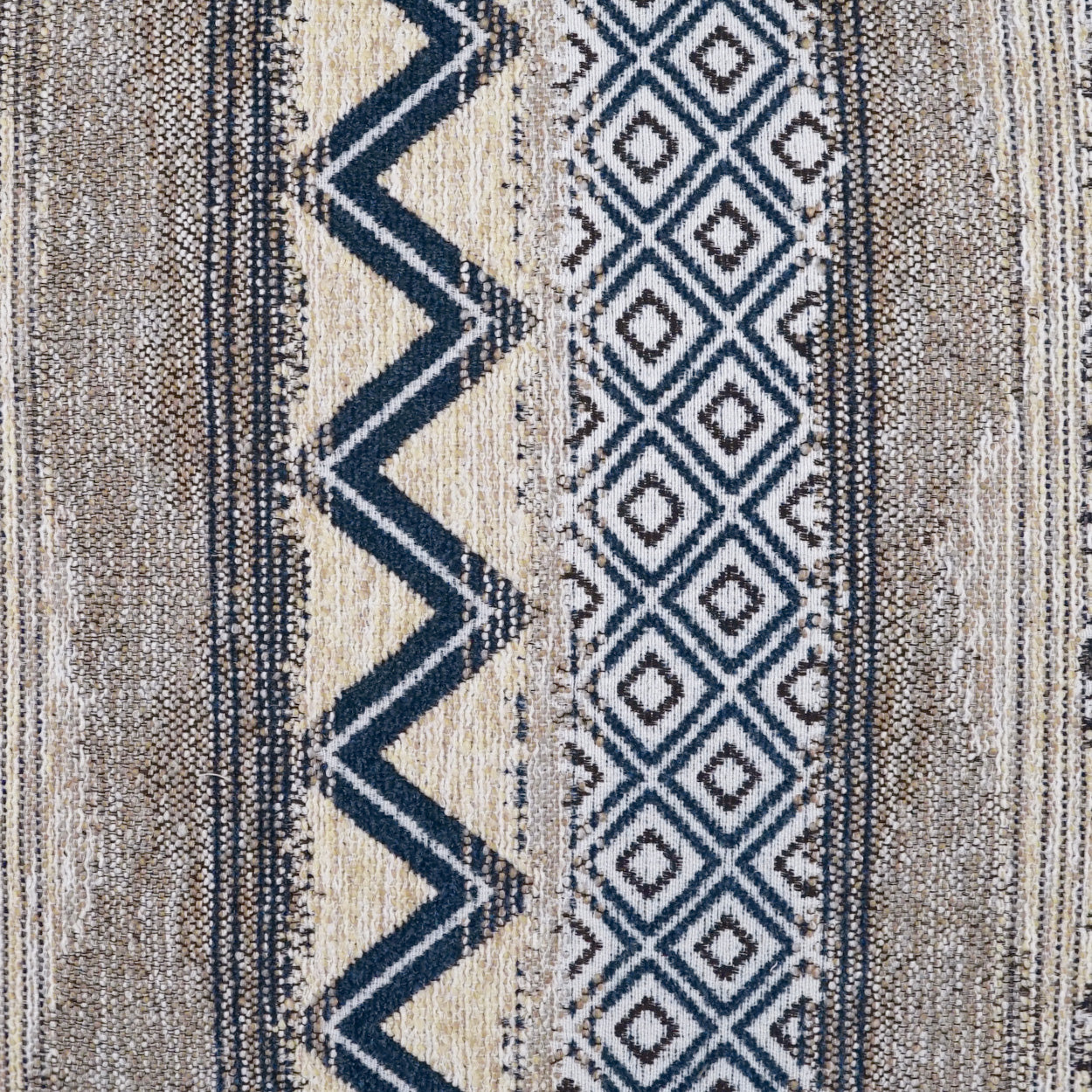 Textured woven rug in beige, tan and navy with zigzag stripe and diamond patterns; boho geometric style for living spaces.