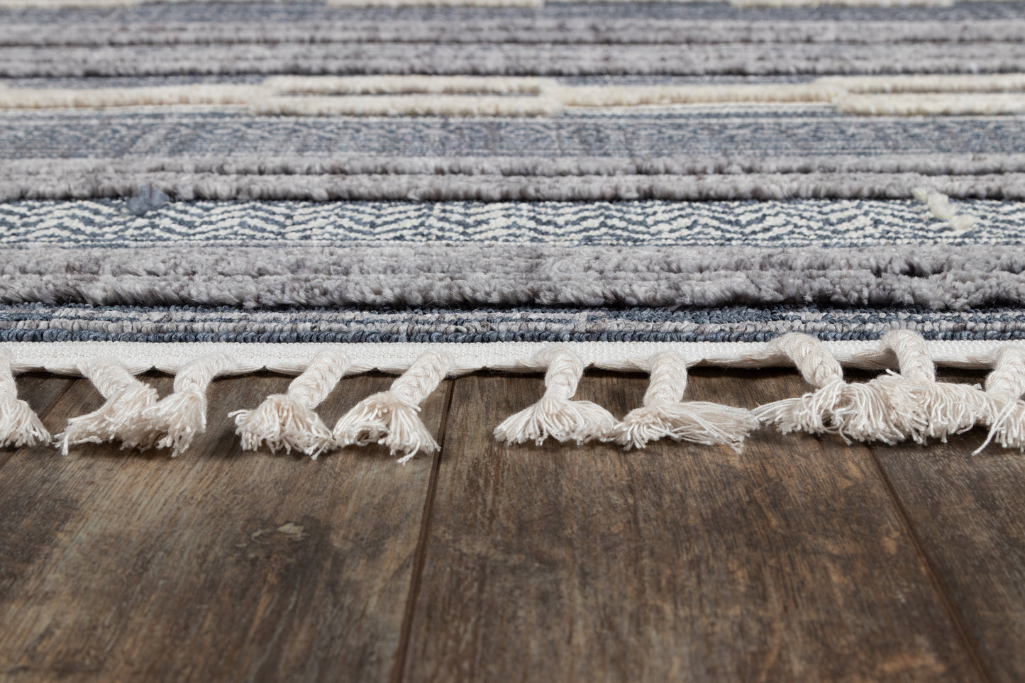 Blue striped rug with cream tassel fringe along edge on a dark wooden floor.