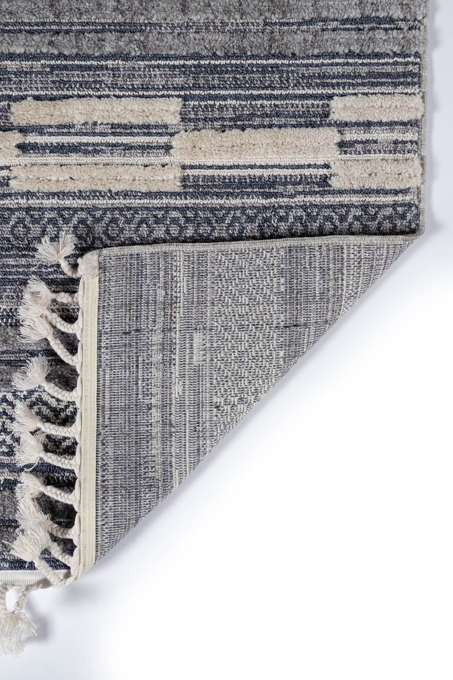 Blue-gray and cream woven area rug with abstract stripe pattern and fringe tassels at edge; folded corner shows underside.