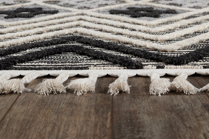 Woven black and white rug with chevron pattern and tassel fringe along edge on a wooden floor.
