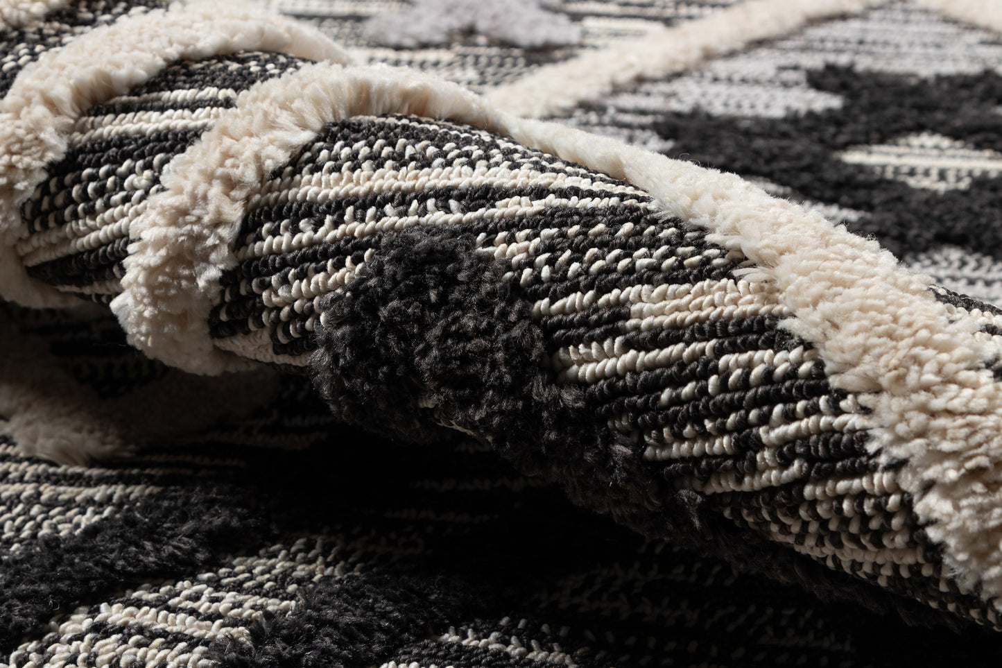 Black and ivory geometric rug with cream fringe; close-up of textured woven pile and folded edge.