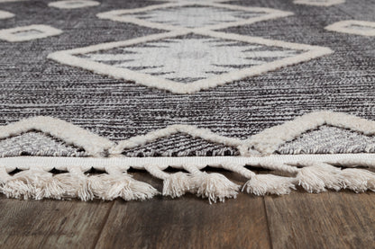 Charcoal gray woven area rug with ivory geometric diamonds and cream fringed edge on wood floor.