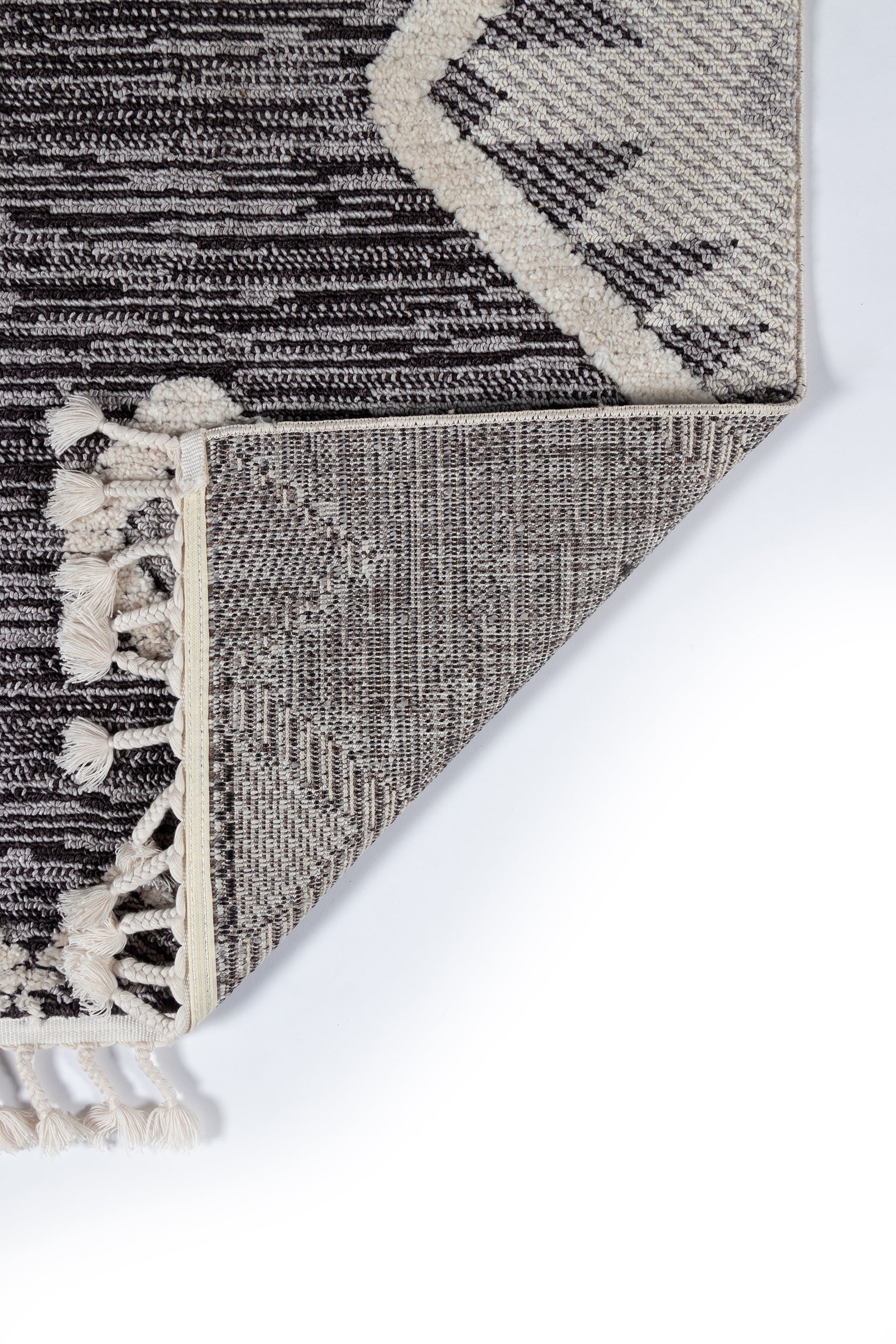 Charcoal and cream geometric rug with tassel fringe, textured woven pattern, folded corner.