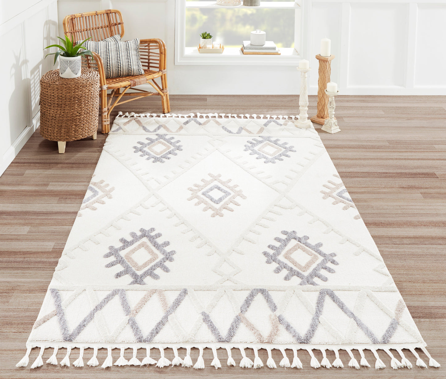 Ivory geometric area rug with tassel fringe and gray diamond motifs in a bright living room with a rattan chair