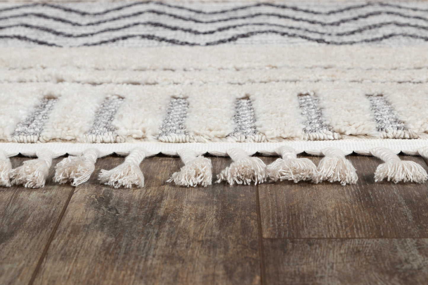 Cream and gray geometric rug with tassel fringe on dark wood floor.