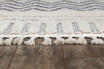 Ivory and gray striped rug with tassel fringe along edge on dark wood floor.