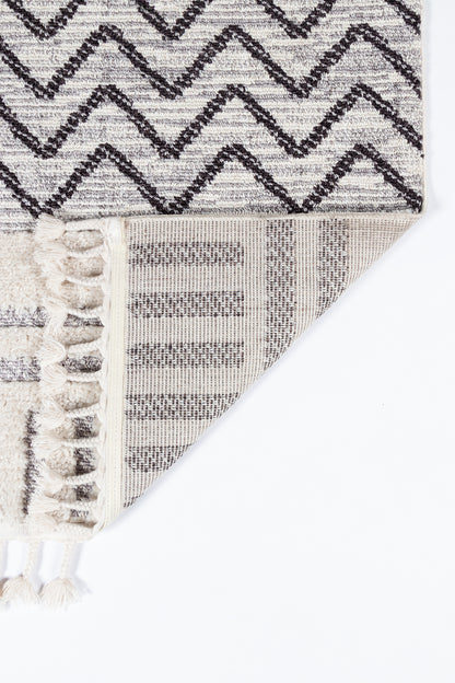 Light gray chevron rug with dark charcoal zigzag pattern, plush woven pile and cream tassel fringe along edge.