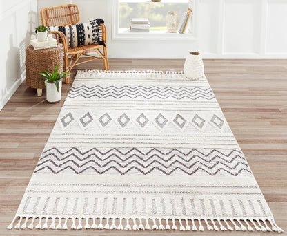Rectangular ivory-and-gray woven rug with geometric diamonds and chevrons, fringe tassels; boho living room decor.