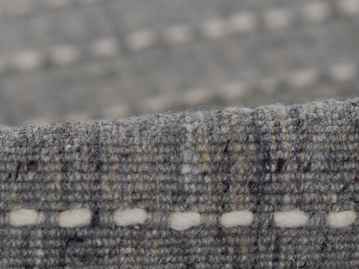 Gray-blue textured wool rug close-up, boucle weave with white oval stitch accents along the edge.