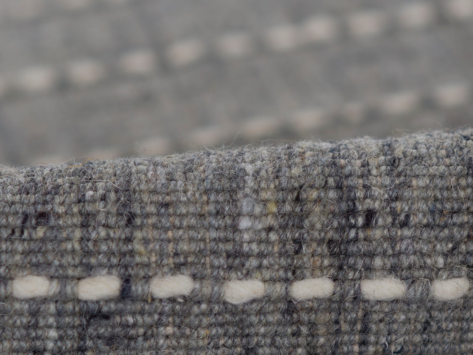Gray-blue textured wool rug close-up, boucle weave with white oval stitch accents along the edge.