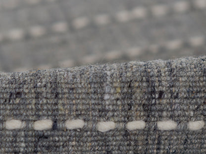 Gray-blue textured wool rug close-up, boucle weave with white oval stitch accents along the edge.