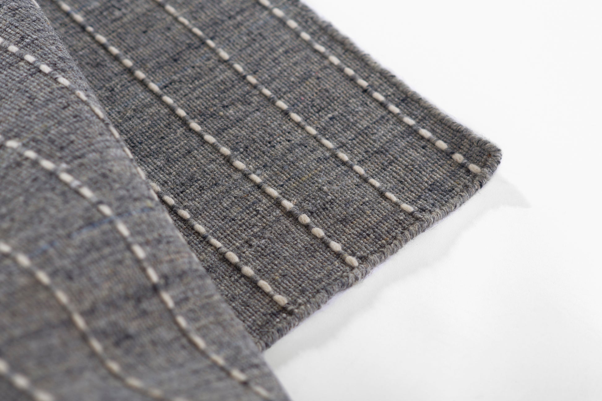 Gray-blue textured rug with white topstitching along a folded edge, denim-style weave.